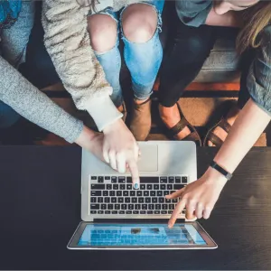 Three people sitting on a couch pointing at a laptop.