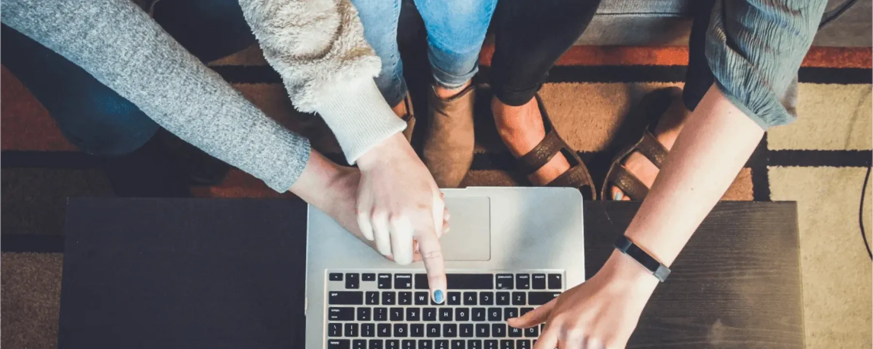 Three people sitting on a couch pointing at a laptop.